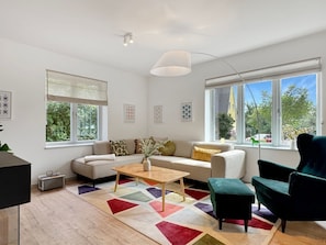 A modern living room with a sofa, a coffee table, and a green armchair. There are large windows with a view of the outside. - Haus Hygge - with sauna and fireplace 1700 - Haus Hygge Am Kurpark with sauna and fireplace 1700 (Dahme)