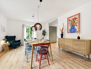 A modern dining area with a wooden table, colorful chairs, and a minimalist cabinet. - Haus Hygge - with sauna and fireplace 1700 - Haus Hygge Am Kurpark with sauna and fireplace 1700 (Dahme)
