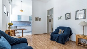 A modern living room with a sofa, a chair, a wooden floor, and a kitchen in the background. - Central Cathedral Apartment (Kotor)