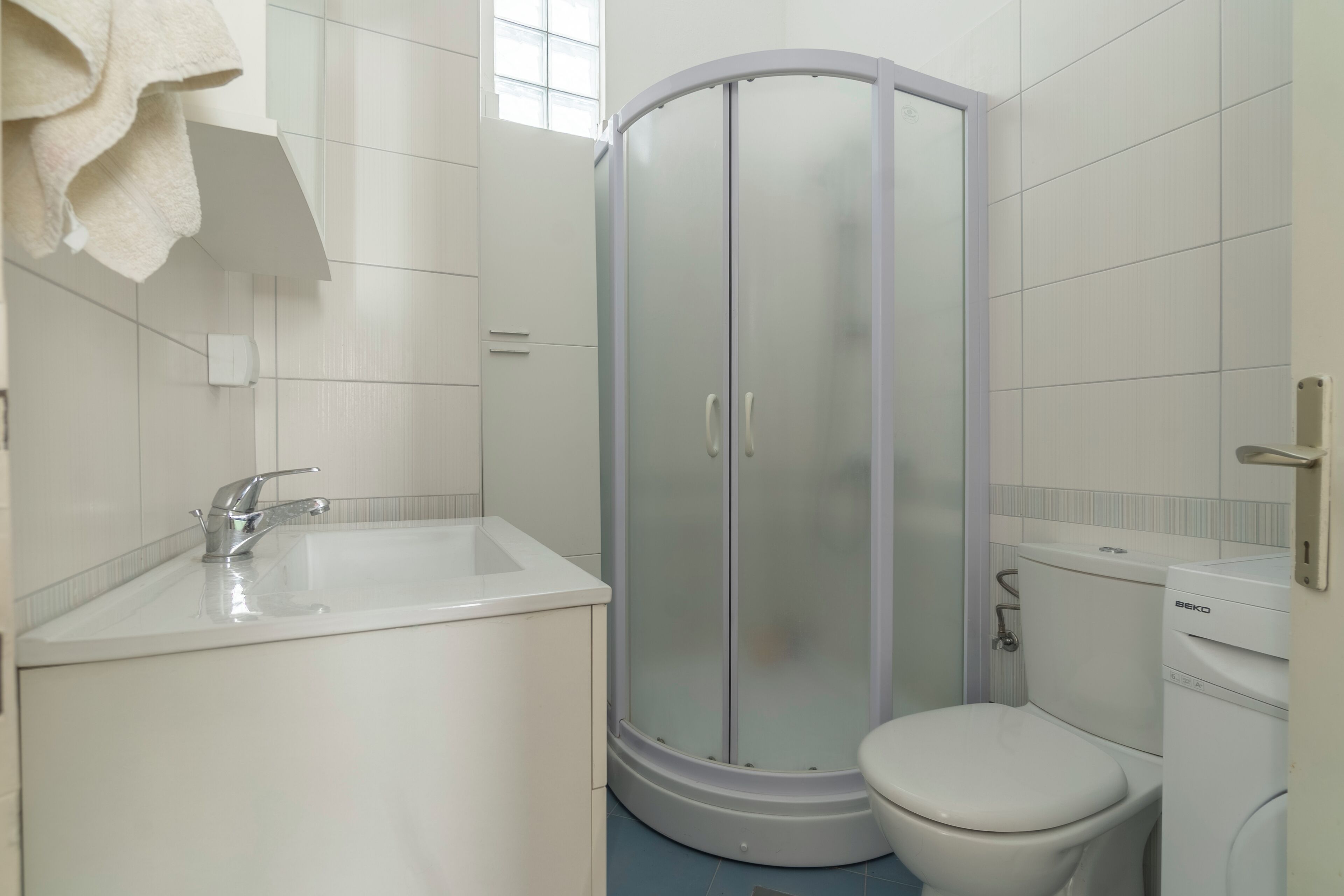 Et badeværelse med bruseniche, toilet, håndvask og et håndklæde hængende på væggen.