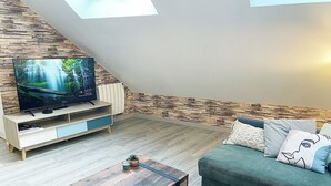 Moderni olohuone, jossa on kiviseinä, litteänäyttöinen televisio, puinen sohvapöytä ja vihreä sohva koristetyynyineen.
