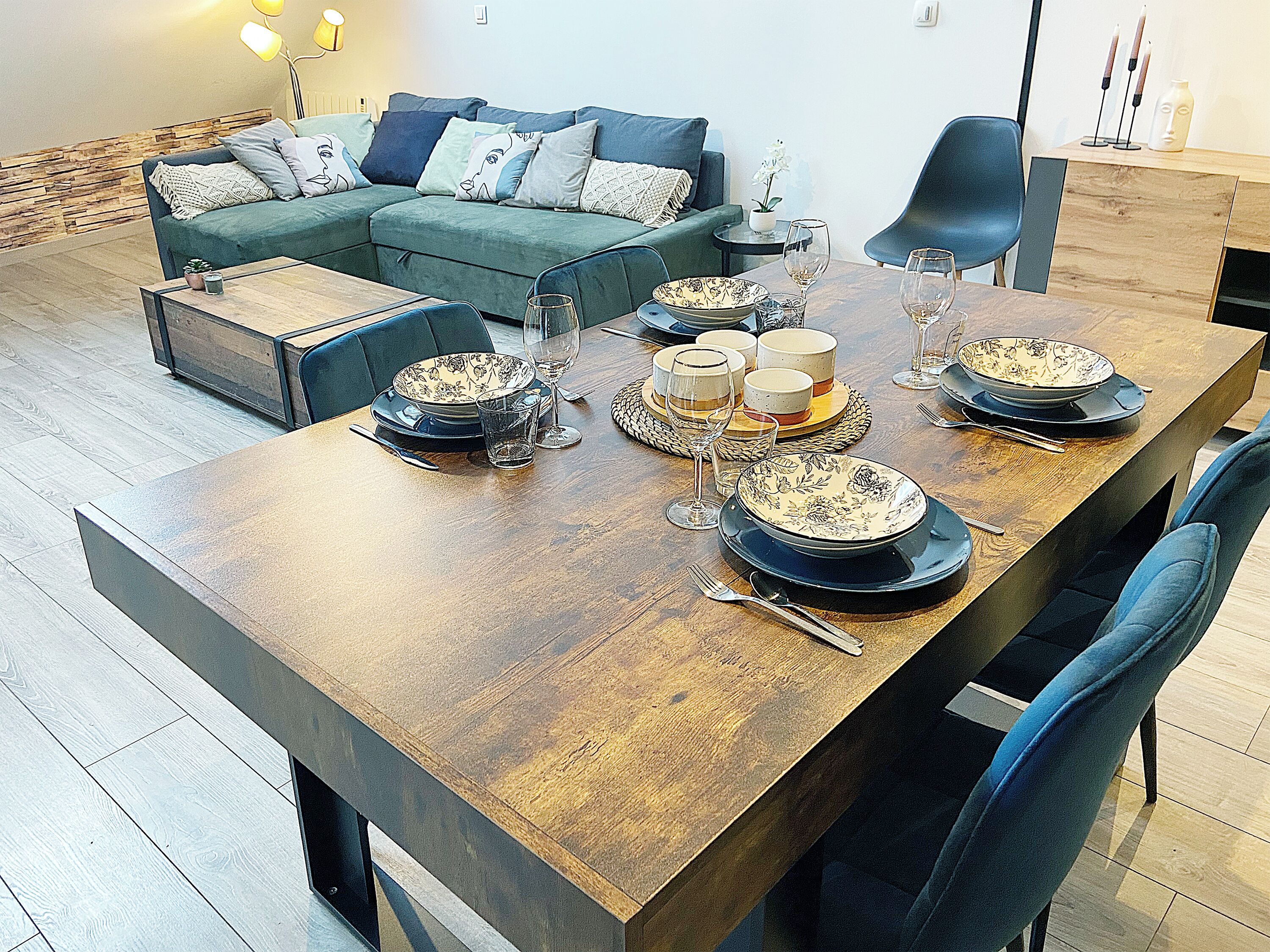 Un coin repas avec une table en bois dressée pour le repas, un canapé et une petite table d’appoint avec une lampe.
