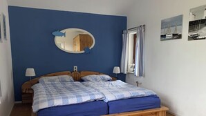 Een slaapkamer met een houten bed, blauwe wanden, een spiegel en twee schilderijen.