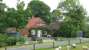 Een landhuis met een rood dak, omgeven door groen en een witte hek.