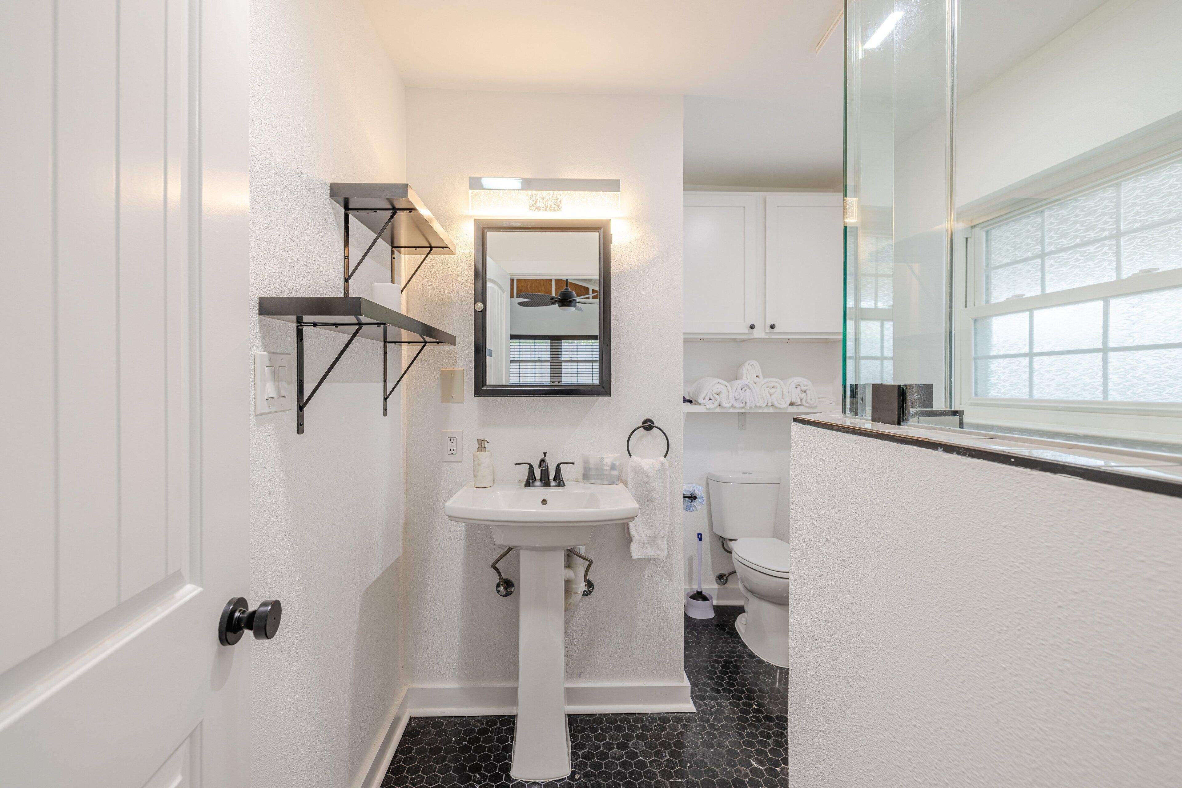 Et lille badeværelse med hvid vask på fod, toilet og brusekabine i glas.