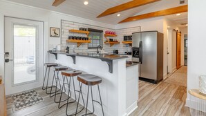 Une cuisine moderne dotée d’un îlot central, de tabourets de bar, de poutres en bois et d’un réfrigérateur en acier inoxydable.