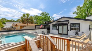 Un jardin avec une piscine, une terrasse en bois et un petit bâtiment doté d’une porte et de fenêtres noires.