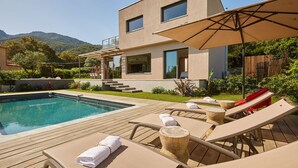 Een modern huis met een zwembad, lounge stoelen en een houten terras.