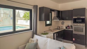 A modern kitchen with dark cabinets, a built-in oven, and a sink. A white sofa with striped pillows is in the foreground. - Casa Barbara (Chania)