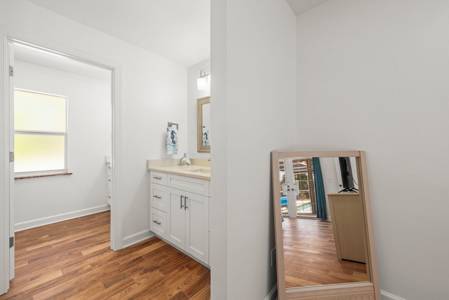 A bathroom with a wooden floor, white cabinets, a sink, and a mirror.