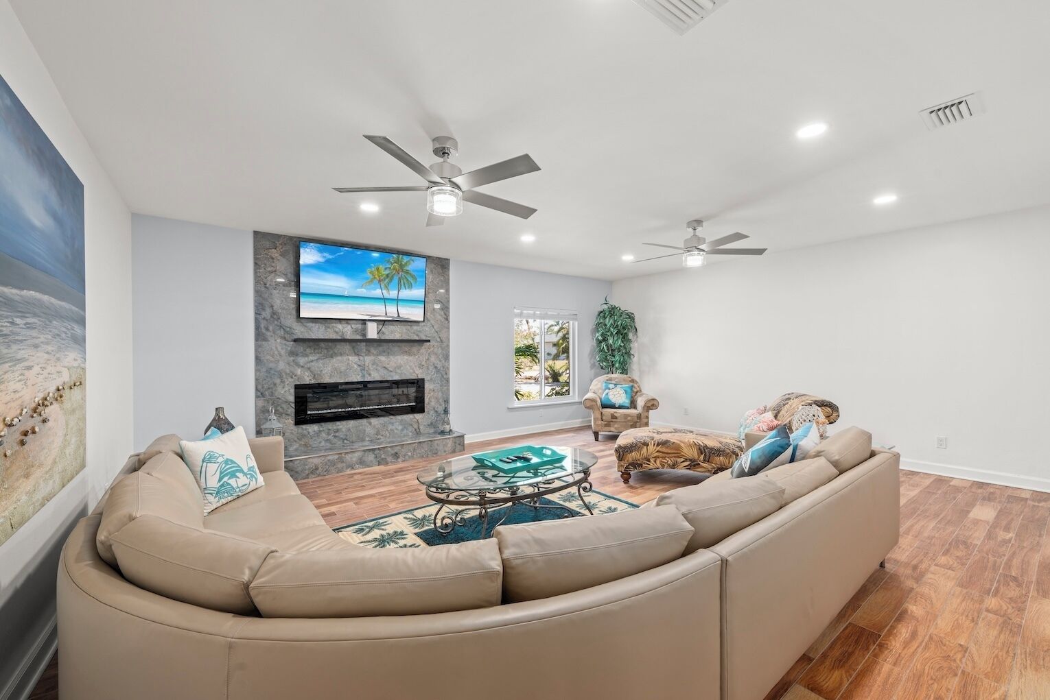 A spacious living room with a large beige sectional sofa, a fireplace, and two ceiling fans.