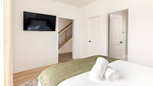 Ein Schlafzimmer mit einem Bett, einem an der Wand montierten Fernseher und einer Treppe, die in einen anderen Raum führt.