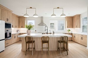 Une cuisine moderne avec des meubles en bois, un îlot central doté de tabourets de bar, une hotte de cuisine en acier inoxydable et des luminaires suspendus.
