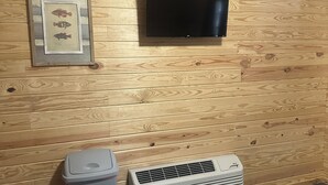 Una habitación con pared de madera, un cuadro de un pez enmarco, un televisor de pantalla plana, un cesto de basura y un equipo de aire acondicionado.