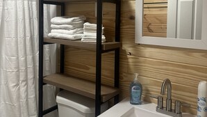 Un baño con pared de madera, un lavamanos blanco, un espejo y un estante con toallas dobladas.