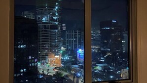 Une vue nocturne sur une ville, capturée à travers une fenêtre, avec des bâtiments illuminés et une rue animée.