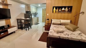 Une chambre d’hôtel moderne avec un lit, une télévision, un bureau et un coin cuisine à l’arrière-plan.