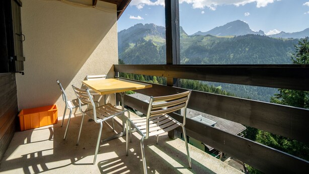 Un balcon avec une table et des chaises, donnant sur un paysage montagneux.