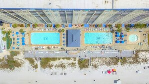 An aerial view of a hotel with multiple swimming pools, sun loungers, and a beach area.