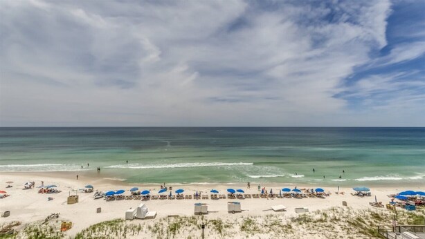 A beach with rows of sunbeds and umbrellas, a sandy shore, and the ocean in the background.