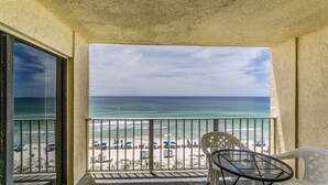 A balcony with a view of the beach, a table, and chairs.