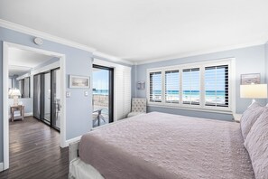 A bedroom with a large bed, a view of the ocean through the window, and a balcony with a chair. - Emerald Towers #205 OnTheGulf*LotsOfResortAmenites (DESTIN)