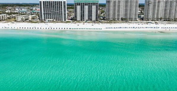 A coastal hotel area with multiple high-rise buildings, a sandy beach, and clear turquoise waters. - Emerald Towers #205 OnTheGulf*LotsOfResortAmenites (DESTIN)