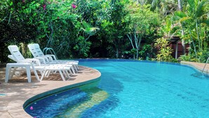 A pool with clear blue water, surrounded by lush greenery and white lounge chairs.