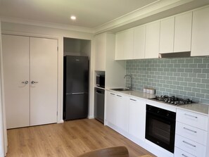Une cuisine moderne avec des meubles blancs, un réfrigérateur noir, un four à micro-ondes, un évier, une cuisinière et un lave-vaisselle.