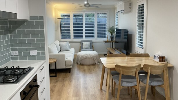 Eine moderne Küche mit einem Gasherd, ein Essbereich mit einem Holztisch und Stühlen, ein Sofa und ein Fernseher.
