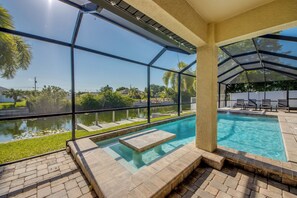 Área de piscina com estrutura de vidro, hidromassagem e vista para um lago e vegetação.