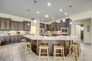 A spacious kitchen with dark wood cabinets, a central island with stools, stainless steel appliances, and pendant lighting.