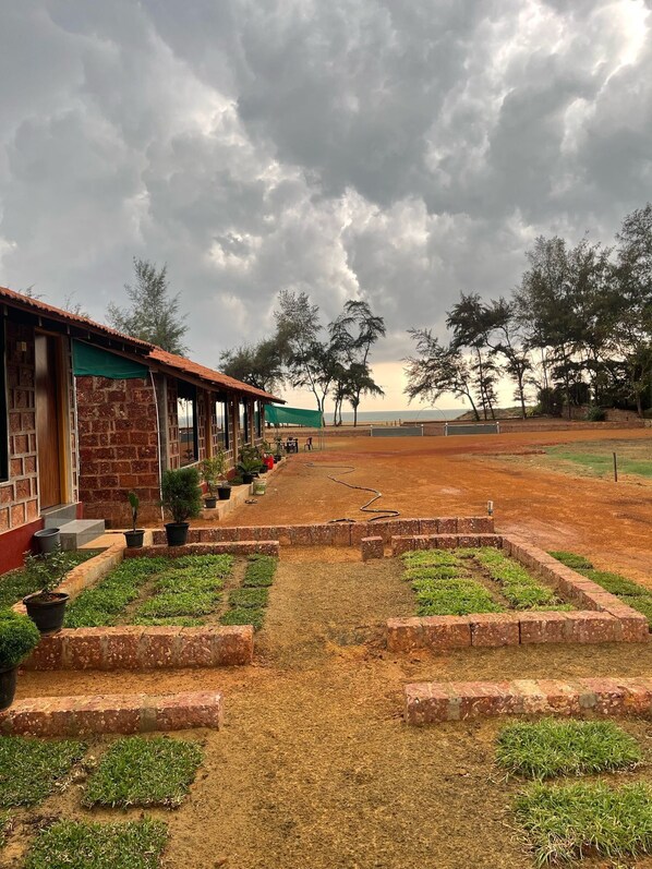A brick building with a green awning, a paved pathway, and a garden area with potted plants. - Blue Waves Beach Stay (Kumta)