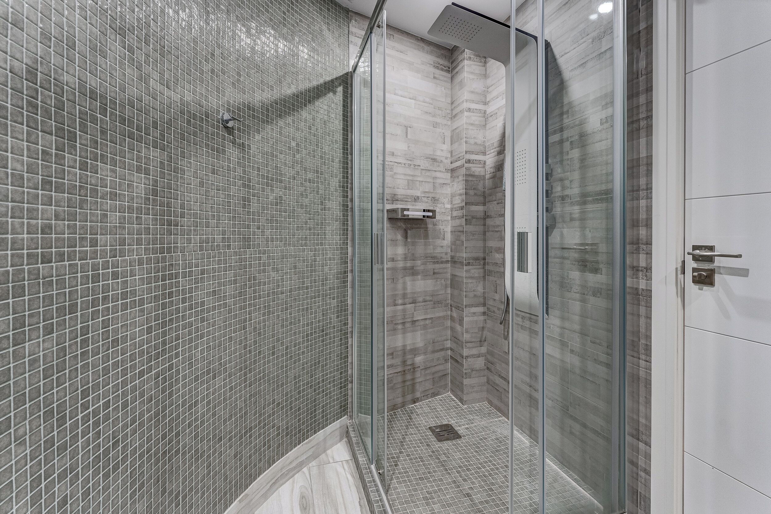 A modern shower area with glass doors, tiled walls, and a marble floor.