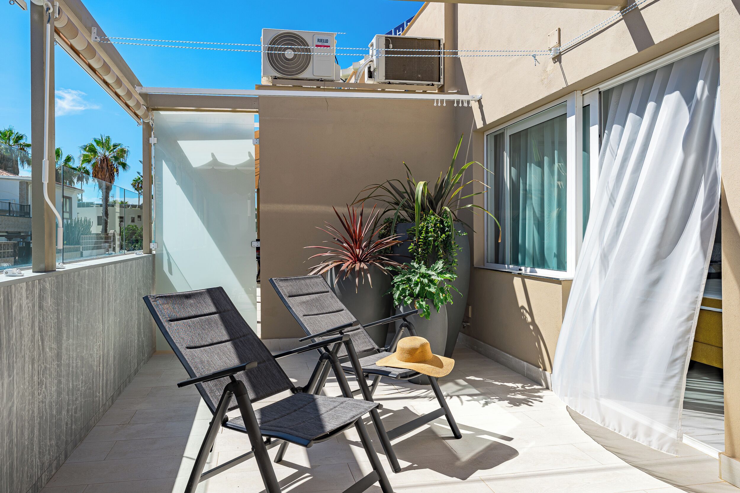 A balcony with two chairs, a potted plant, and a sun hat.