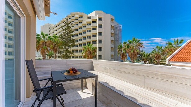 A balcony with a table and chairs, a fruit bowl, and a view of high-rise buildings and palm trees. - BAL Apartments - Adults Only (Arona)