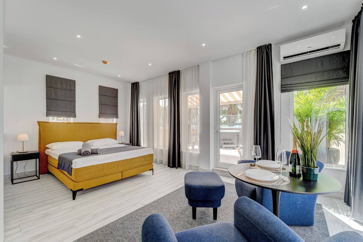 Una habitación de hotel moderna con cama, zona de comedor y vistas a zonas verdes.