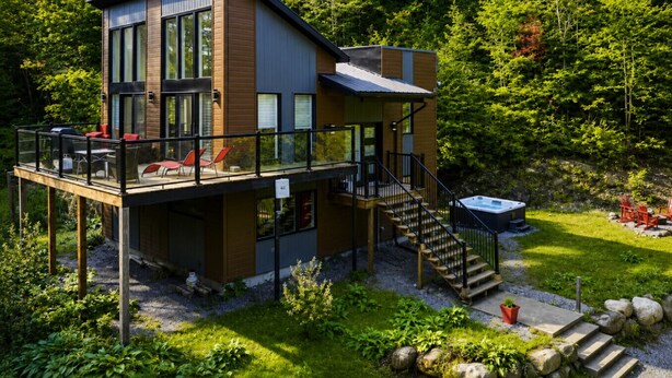 Une maison moderne à deux étages dotée d’une terrasse, d’un espace salon extérieur et d’un jacuzzi.