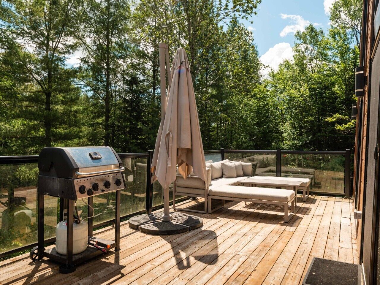 An outdoor deck with a grill, a covered umbrella, and a sofa with cushions.