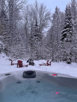 A hot tub surrounded by snow-covered trees and red Adirondack chairs. - La Clairière Enchantée, Spa et Bord de L`Eau (Chertsey)