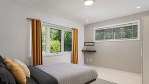 Un dormitorio con cama, una ventana con cortinas, una mesita de noche y un estante en la pared.