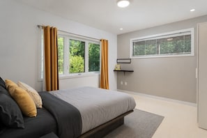 A bedroom with a bed, a window with curtains, a bedside table, and a wall-mounted shelf.