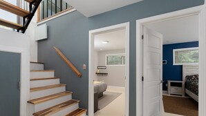 Un interior moderno con una escalera, un dormitorio con cama y mesita de noche, y un pasillo que conduce a otra habitación.