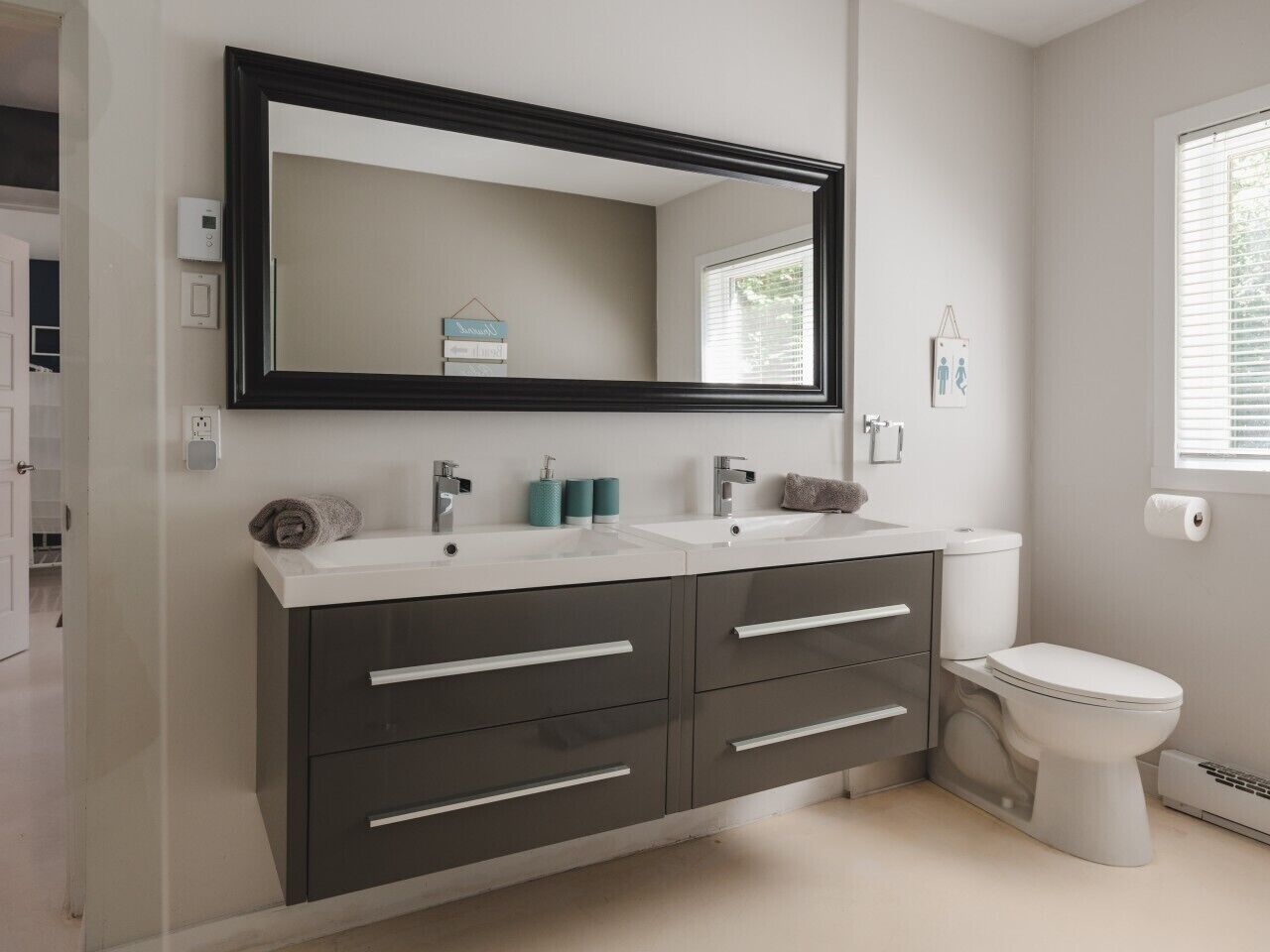 A bathroom with a dark-colored vanity, two sinks, a toilet, and a large mirror.