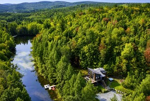 A cabin surrounded by dense forest, a river, and a dock with a boat. - La Clairière Enchantée, Spa et Bord de L`Eau (Chertsey)