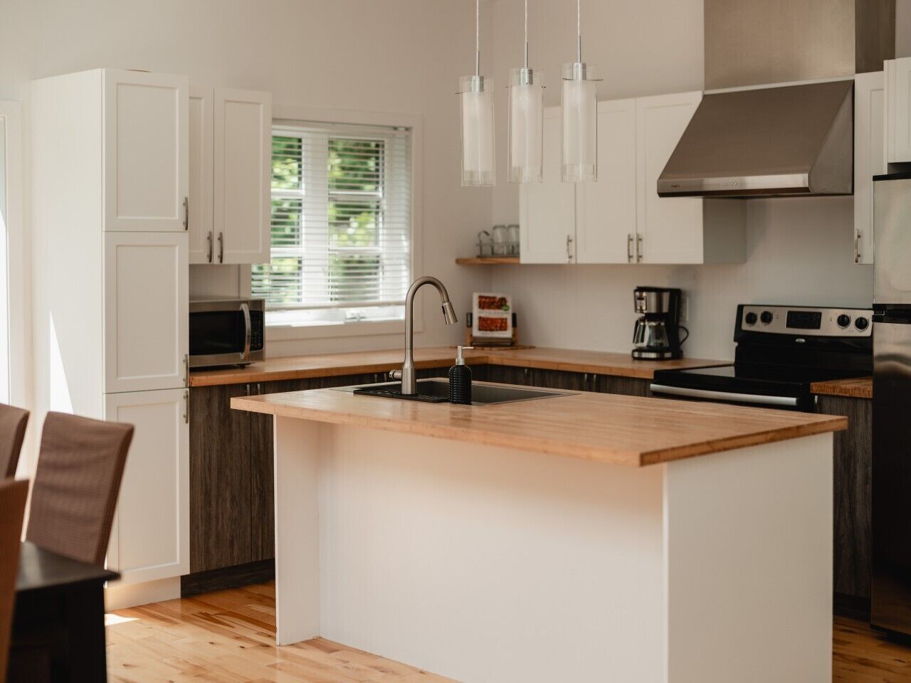 Una cocina moderna con armarios blancos, una isla de madera con pileta y electrodomésticos de acero inoxidable, además de lámparas colgantes.