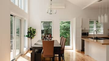 A modern kitchen with a dining area, large windows, and a view of greenery.