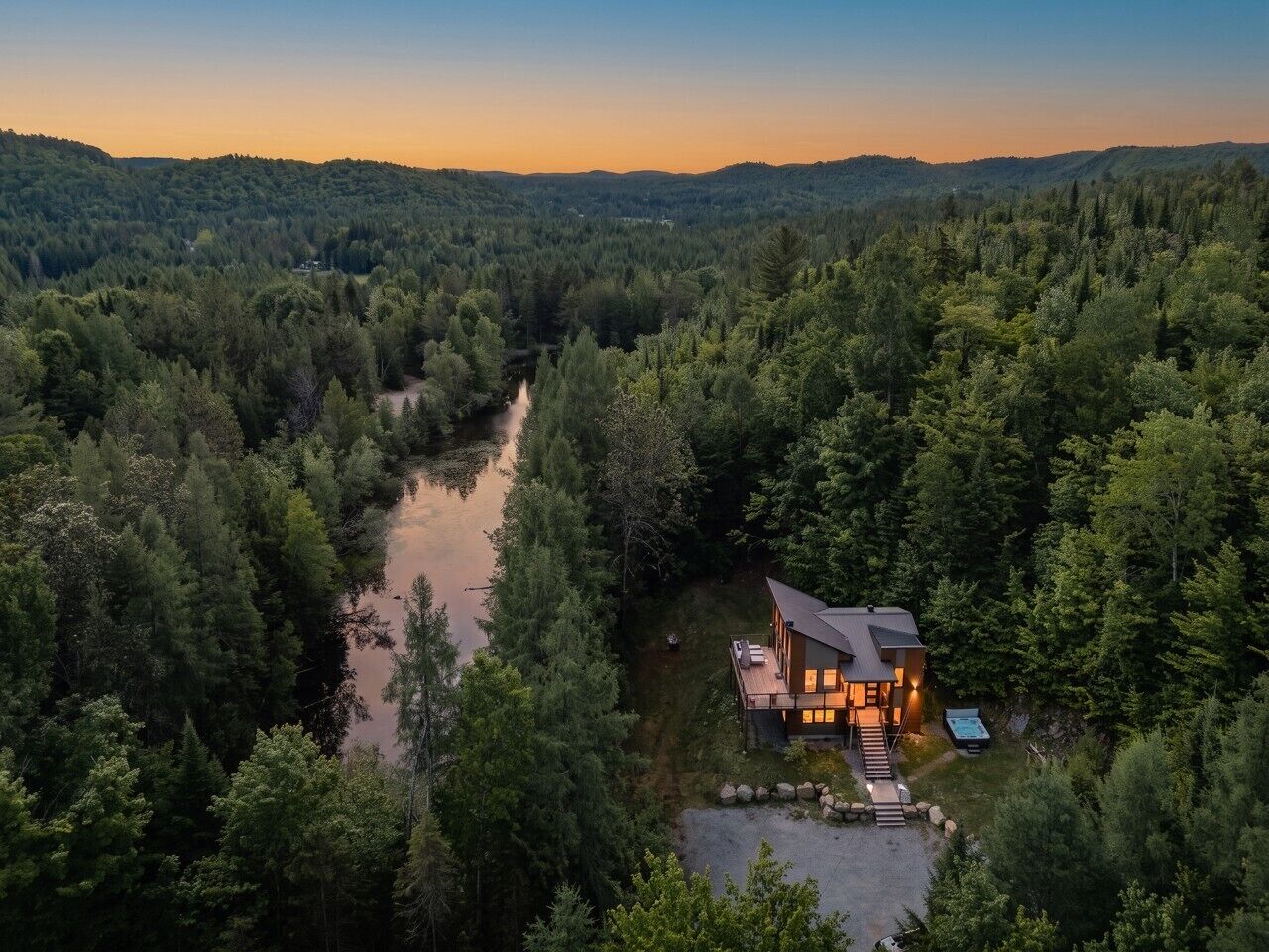 Eine Hütte, umgeben von dichtem Wald, mit einem Fluss im Vordergrund.