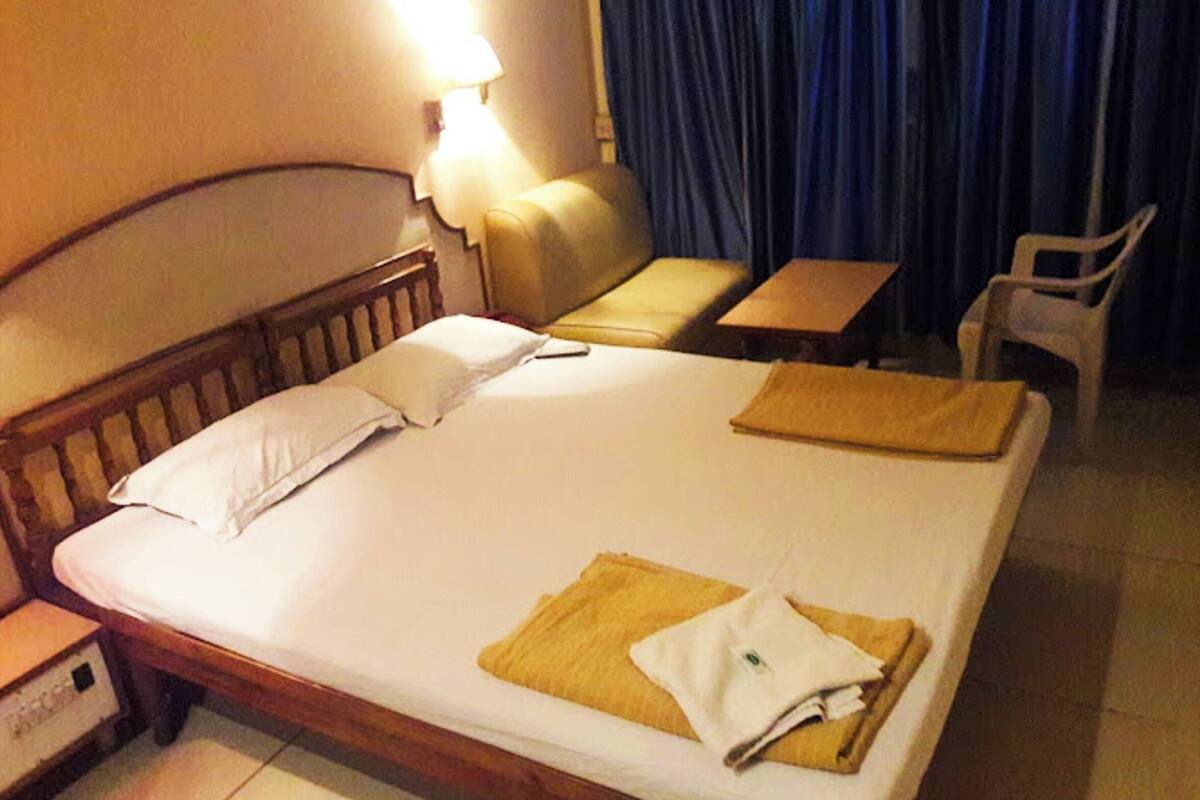 A hotel room with a bed, a nightstand, a lamp, a sofa, a small table, and a chair.