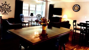 A dining area with a wooden table, chairs, a vase with flowers, a ceiling fan, and a wall-mounted clock. - Ocean view 5-bedroom house in Narragansett with AC, WiFi, beach pass (Narragansett)